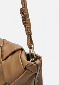 Brązowa skórzana torebka z plecionym uchwytem i złotymi akcentami. Torba ma miękką, fakturowaną powierzchnię z marszczonymi sekcjami.