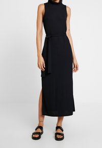 Czarna długa sukienka bez rękawów z wysokim dekoltem, paskiem w talii i rozcięciem po bokach. Wykonana z gładkiej, lekkiej tkaniny.