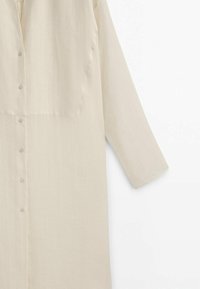Chemise longue beige à boutons avec manches longues en tissu léger.