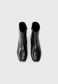 Botas de tobillo de cuero negro con una textura suave, diseño de punta cuadrada y cierre con cremallera lateral, que presentan una silueta minimalista y elegante.