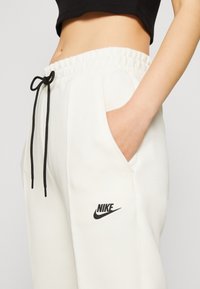 Pantalon de survêtement blanc Nike avec taille à cordon, poches latérales et logo noir. Texture lisse et coupe décontractée.