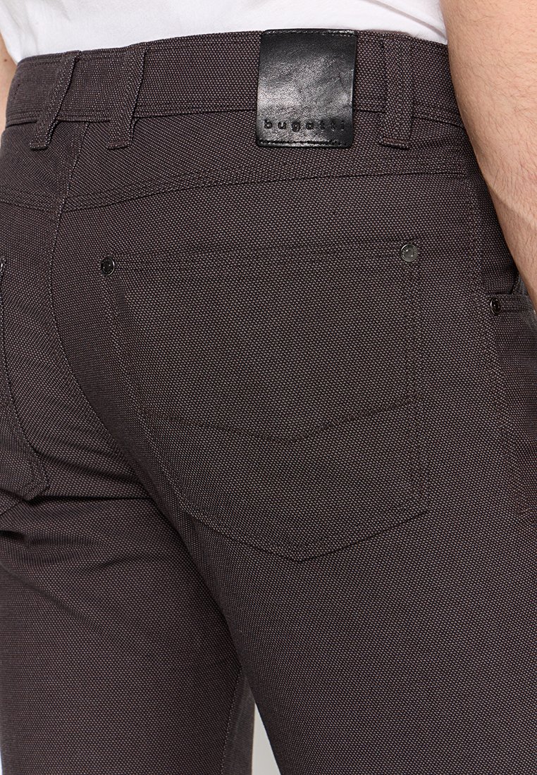 Nahaufnahme von dunklen strukturierten Hosen mit Details an der Gesäßtasche und einem schwarzen Leder-Label mit der Aufschrift "bugatti" am Bund.