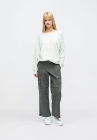 Helehall hall, kergelt üle suuruse, dressipluus tumeda halli lahtiste pükstega, mis on varustatud mitme taskuga, ning valgete spordijalatsitega.