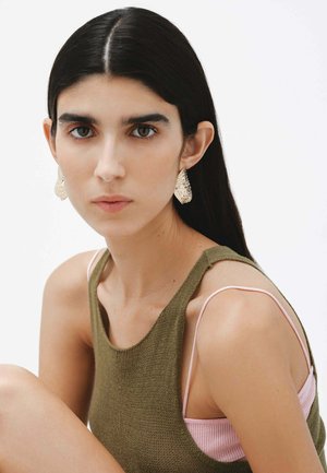 Pendientes texturizados en oro, top de punto verde oliva y tirantes rosa claro. Fondo neutro, centrado en los detalles de los accesorios y la prenda.