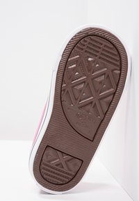 Sneaker in tela rosa con suola in gomma bianca. La suola presenta un motivo a trama geometrica per una migliore aderenza. È visibile il marchio del produttore.