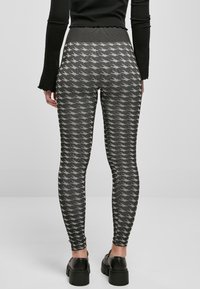 Leggings i houndstooth-mønster, med høy midje og et strukturelt strikket stoff i nyanser av svart og grått. Enkle svarte sko er synlige.