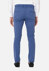 Pantaloni in cotone blu a chino con vestibilità slim, dotati di tasche posteriori con bottone e una finitura leggermente testurizzata. Indossati con sneakers nere.