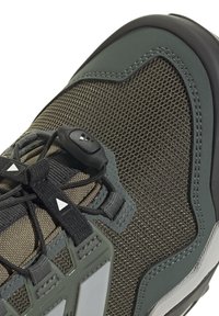 Nära bild av en grön och svart vandringsko med meshmaterial, syntetiska överlägg och ett snabb-snörningssystem med plastspärr.