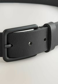 Ceinture en cuir noir avec une finition texturée, dotée d'une boucle en métal rectangulaire de couleur noir mat, et de plusieurs trous de réglage le long de la ceinture.