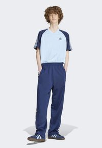 Jersey de cuello en V azul claro con mangas oscuras, pantalones deportivos marinos y zapatillas deportivas azules con tres franjas blancas y acentos de logotipo.
