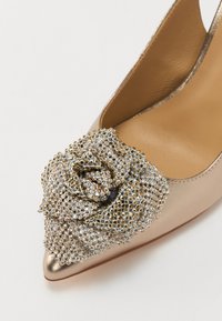 Zapato de piel con un acabado metálico en tono rosa y punta afilada, que presenta un acento de rosa joya hecho de strass claros y en tono dorado.