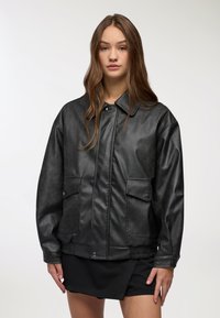 Giacca in pelle sintetica nera con colletto a punta, due tasche frontali e orlo arricciato. Tessuto morbido e vestibilità leggermente oversize.