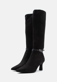 Μαύρες μπότες από σουέντ με ψηλό τακούνι, μυτερή μύτη και κομψό, ψηλό κορμό. Διαθέτουν στενό μαύρο δερμάτινο λουράκι με μεταλλική αγκράφα.