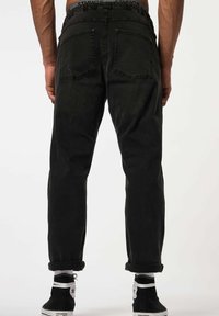 Jeans de mezclilla negra con corte relajado, cinturilla elástica, puños enrollados y dos bolsillos traseros. Tejido texturizado con un detalle mínimo.