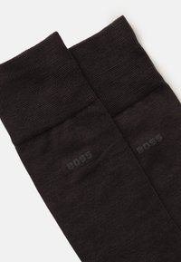 Meias castanhas escuras com punhos canelados, feitas de um material texturizado. Apresentam uma subtil marca "BOSS" em cinza em cada meia.