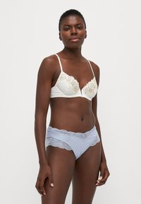 Soutien-gorge blanc avec bordure en dentelle et bretelles réglables, associé à un slip bleu clair avec des accents en dentelle. Tissu lisse, design classique, détails féminins.