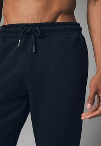 Schwarze Jogginghosen aus weichem Stoff, mit einem elastischen Bund und Kordelzug sowie dezenten Seitentaschen. Glatte Textur.