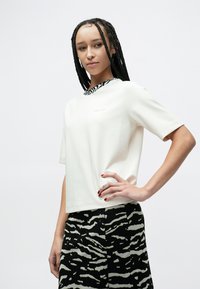 Baltas trumpomis rankovėmis viršus su tekstūruotu juodai baltu raštuotu apykakle, derančiu su juoda sijonu, kuriame yra kontrastingas zebro dryžių dizainas.