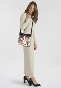 Crossbody-Tasche mit schwarzem Oberteil, das pastellfarbene Kunstwerke eines Mädchens und Akzente mit Punkten zeigt. Verstellbarer Riemen, glatte Textur und sichere Verschluss.