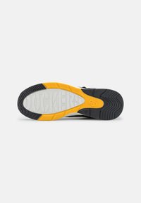 Semelle de sneaker noire et grise avec un accent jaune, présentant un motif en caoutchouc blanc texturé et des rainures pour l'adhérence.