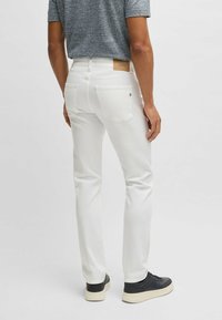 Białe dżinsy denimowe o dopasowanym kroju, z tylnymi kieszeniami i skórzaną naszywką z logo. Połączone z czarnymi sneakersami z białymi podeszwami.