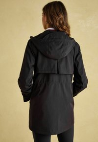 Czarna wodoodporna kurtka z kapturem, z wentylacją z tyłu, długimi rękawami i średniej długości krojem. Gładka tekstura, minimalistyczny design.