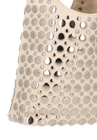 Beżowa skórzana torebka o fakturowanej powierzchni, zdobiona lustrzanymi metalicznymi okrągłymi akcentami w różnych rozmiarach. Duże zamknięcie u góry.