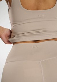 Beige träningsset bestående av en tanktop och leggings med en slät, elastisk textur. Diskret "S/B"-logotyp broderad på båda delarna.