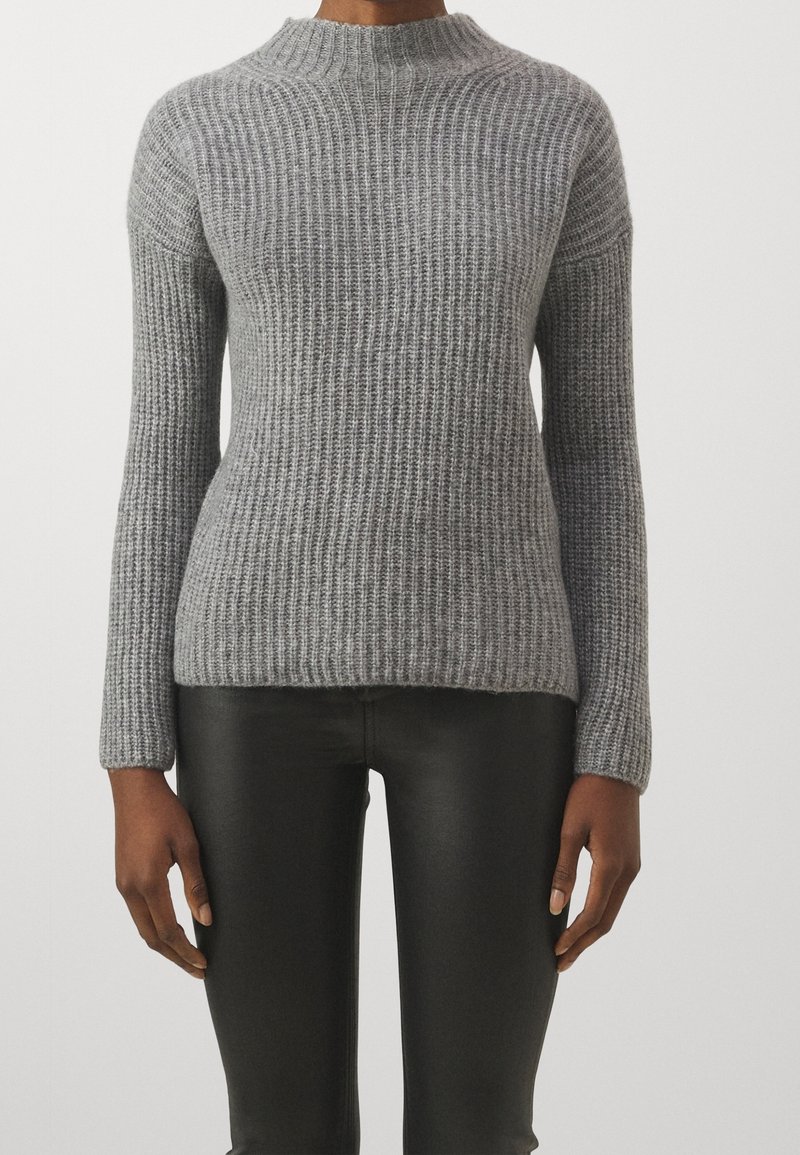 Maglione grigio in maglia a coste con collo alto, maniche lunghe e vestibilità comoda, abbinato a pantaloni neri aderenti. Aspetto testurizzato e accogliente.