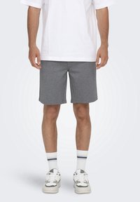 Pantaloni sportivi grigi realizzati in tessuto morbido, con una vestibilità rilassata, una texture liscia e un taglio dritto. Indossati con una maglietta bianca e scarpe da ginnastica.