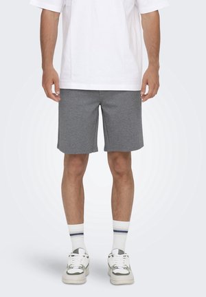 Shorts de sport gris en tissu doux, présentant une coupe décontractée, une texture lisse et une coupe droite. Portés avec un t-shirt blanc et des baskets.