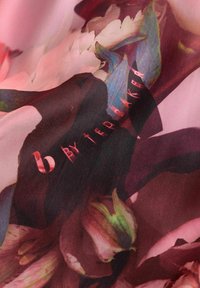 Ľahká tkanina s kvetinovým vzorom v ružových a tmavých odtieňoch, ktorá zobrazuje hladkú textúru so subtílnym leskom a potlačeným detailom loga.