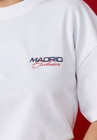 White t-shirt showing black and red text reading "Madrid Exclusive" on chest against a red background.