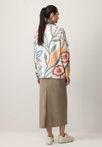 Suéter de punto con estampado floral multicolor y mangas largas, combinado con una falda beige de largo medio. El fondo es neutro y claro.