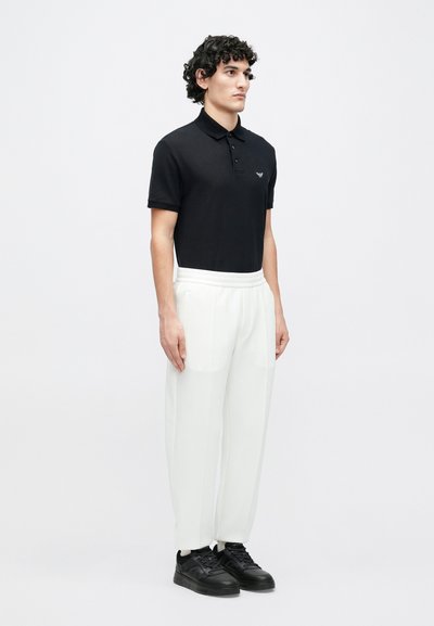 Čierne polokošeľa s golierom a malým logom, v kombinácii s bielymi zúženými nohavicami a čiernymi teniskami. Hladká látka a pohodlný strih.