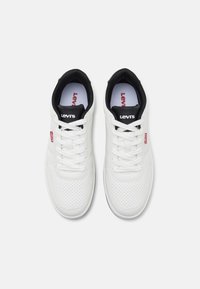 Vita sneakers i perforerat läder med svarta accenter. Funktioner inkluderar platta skosnören och en logotyp på tungan och sidan.