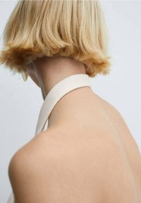 Blond włosy o prostym cięciu, miękka tekstura. Odsłonięte plecy z szerokim, jasnym paskiem. Prosty, minimalistyczny design na neutralnym tle.