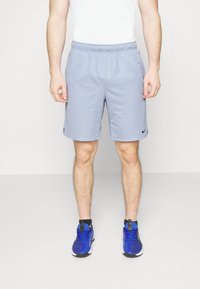 Pantalones cortos deportivos azul claro hechos de tela suave, con una cinturilla elástica y un pequeño logo negro de Nike. Combinados con zapatillas azules.