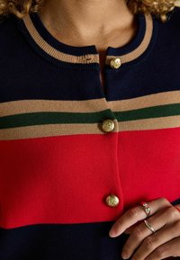 Strickjacke mit horizontalen Streifen in Marineblau, Rot und Beige. Goldene Knopfverschlüsse mit strukturiertem Detail. Glatte Stricktextur.