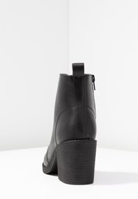 Bottine noire à talon incurvé, texture en cuir lisse, avec une fermeture éclair latérale et une bande d'extraction à l'arrière pour un enfilage facile.