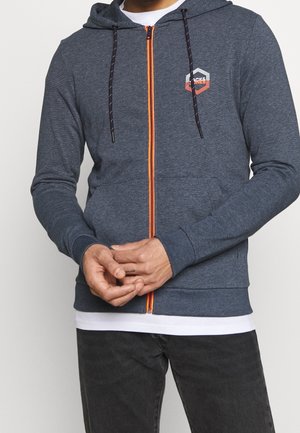 Sudadera con cremallera de tela gris oscuro con cremallera naranja en contraste, cordones estampados y bolsillos frontales. Presenta un logo en el pecho.