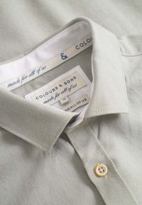 Helles graues Hemd mit Kragen aus strukturiertem Stoff, mit Knopfverschluss und Etiketten mit der Aufschrift "Colours & Sons" und "made for all of us."