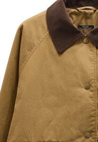 Brązowa bawełniana kurtka z kołnierzem z sztruksu, zapinana na zatrzaski i o gładkiej fakturze. Charakteryzuje się lekko oversize'owym krojem.
