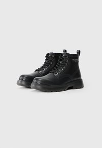 Botine negre cu șireturi, din piele, având o talpă groasă, vârf rotund și o ochetă în partea din spate. Etichetă de marcă pe accentul lateral.