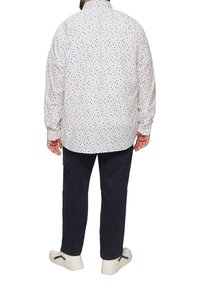 Wit overhemd met lange mouwen en kleine veelkleurige stippen, met knopenmanchetten en een afgeronde zoom, gecombineerd met donkere broek en witte schoenen.