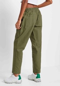 Vapaat, oliivinvihreät housut, joissa on joustava vyötärönauha ja kaksi takataskua. Yhdistetty valkoisiin lenkkareihin, joissa on vihreitä yksityiskohtia.