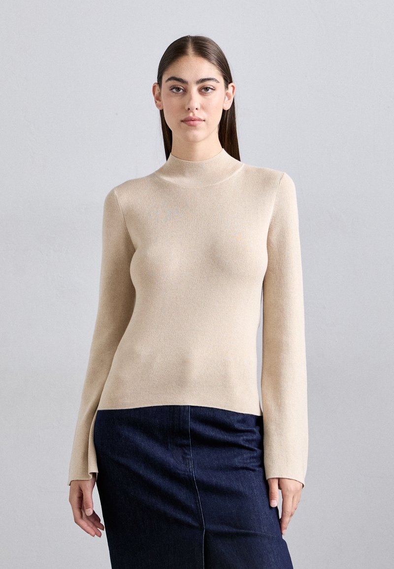 Pulover bej cu mâneci lungi și design cu guler înalt ajustat. Textură moale, cu dungi, asortat cu o fustă din denim închis la culoare, cu o siluetă ajustată.