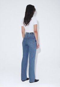 Jeans de denim azul de tiro alto, con corte recto, que cuentan con dos bolsillos traseros y una etiqueta de marca negra en la cintura.