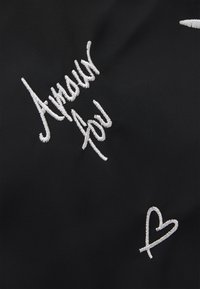 Schwarzer Stoff mit weiß gesticktem Text, der "Amour pour" und ein kleines Herzdesign enthält, und so die glatte Textur und kontrastierenden Farben hervorhebt.