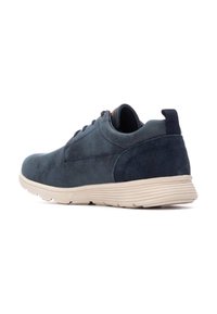 Zapatilla deportiva de ante azul marino con parte superior texturizada, suela ligera color beige, punta redondeada y lengüeta trasera. Diseño suave y minimalista.